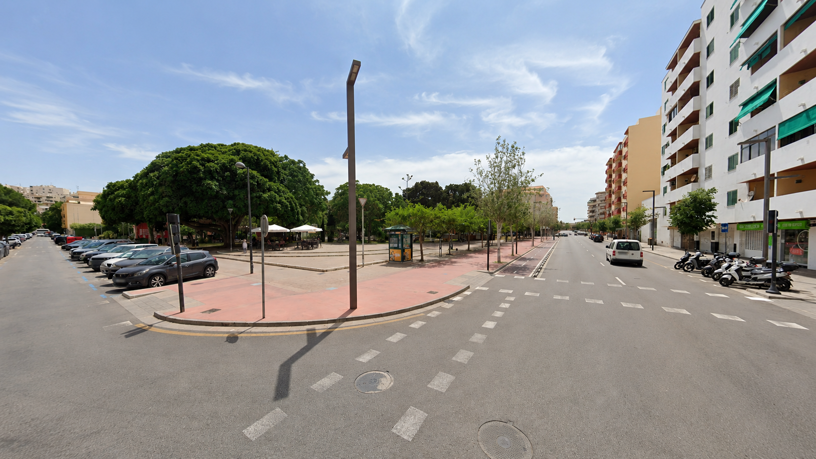 Kruispunt in Ibiza Stad met groen plein en geparkeerde auto's